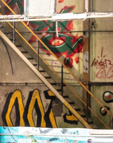 Trap met gele leuning naast een muurschildering en graffiti in een vervallen ruimte.
